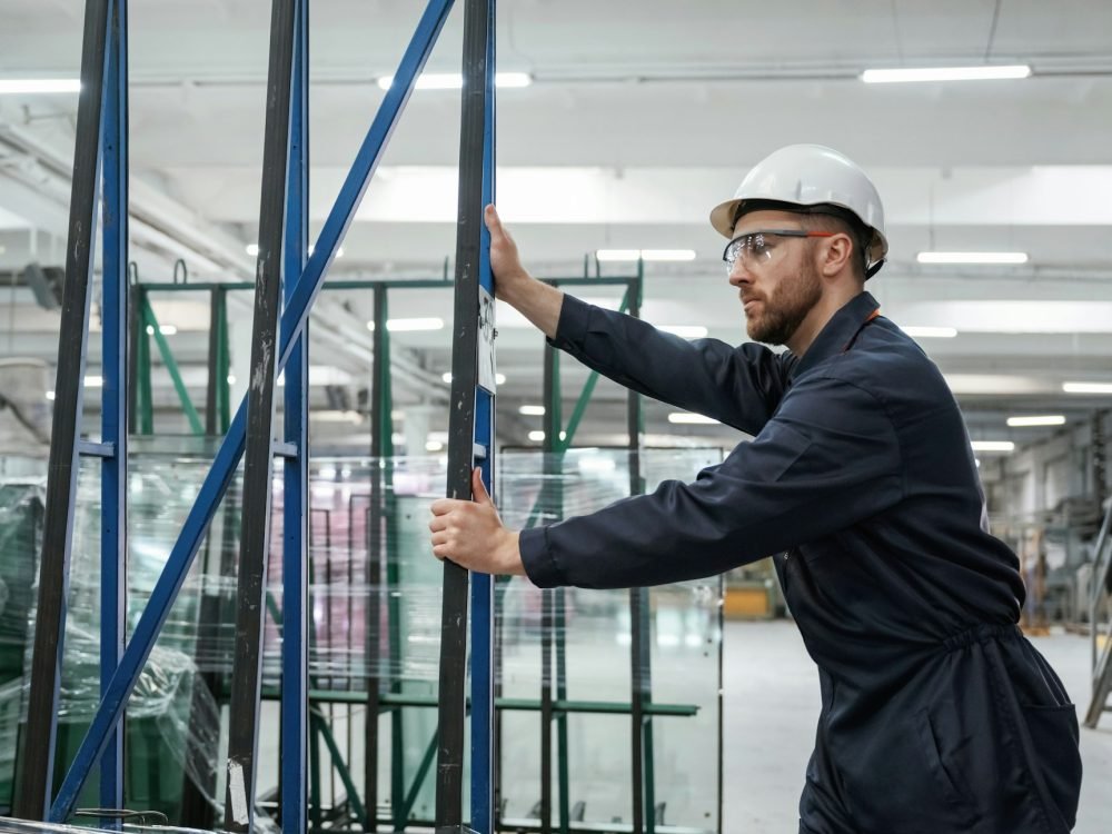 Moving the parts of windows. Factory worker is indoors with hard hat